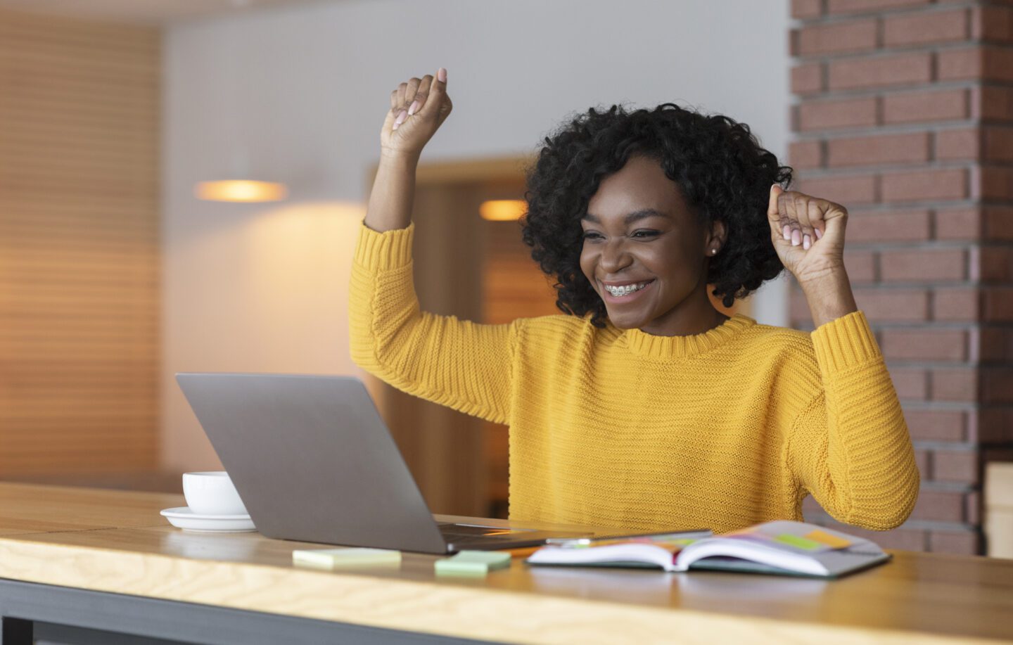 Black girl celebrating success in front of laptop at cafe, clenching fists and screaming, found good job, copy space